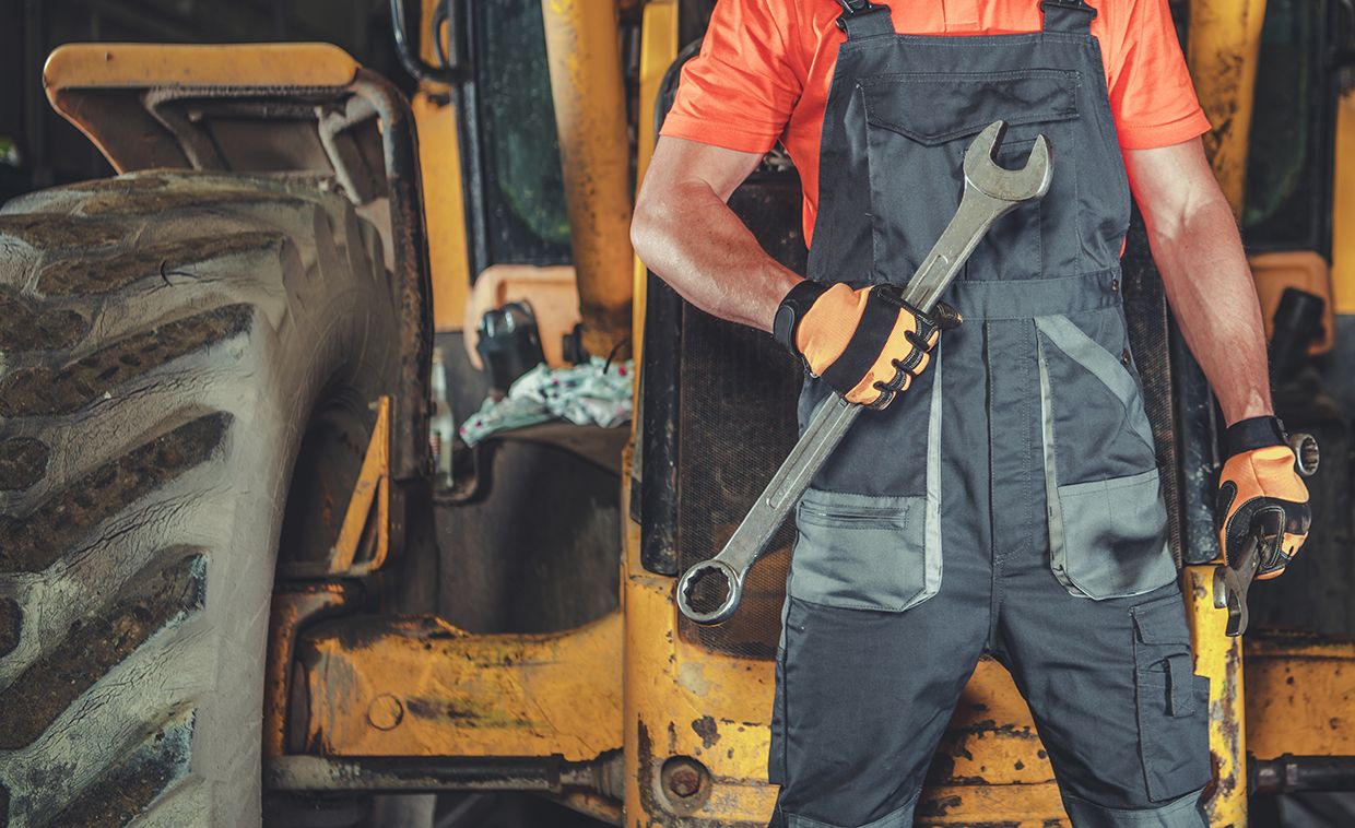Mann in Arbeitshose mit großem Schraubenschlüssel vor Maschine.