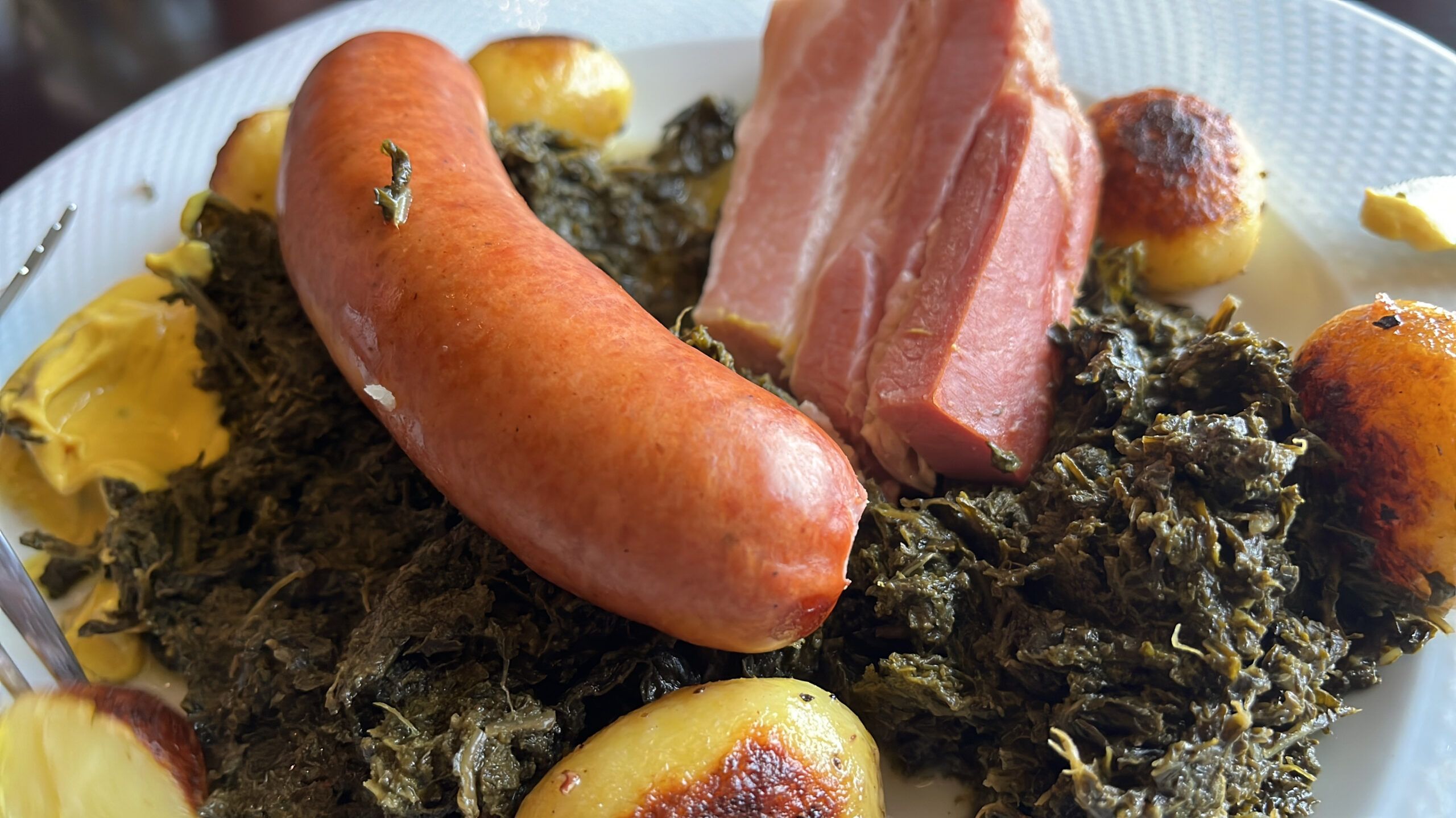 Teller mit Grünkohl, Kasseler, Kohlwurst und karamellisierten Kartoffeln.